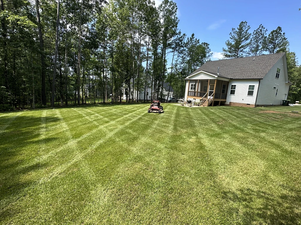 Grass Geeks mower on a freshly striped backyard lawn behind a home