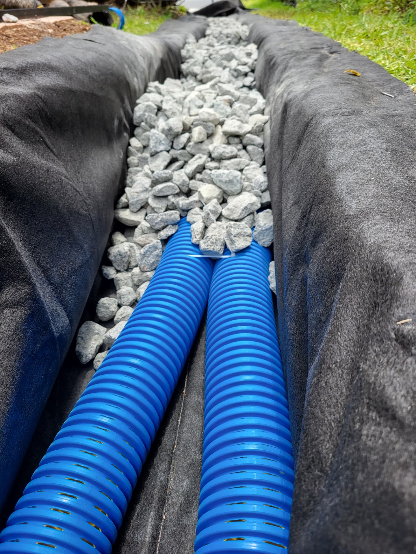 French drain installation with perforated pipe, gravel and filter fabric in a trench