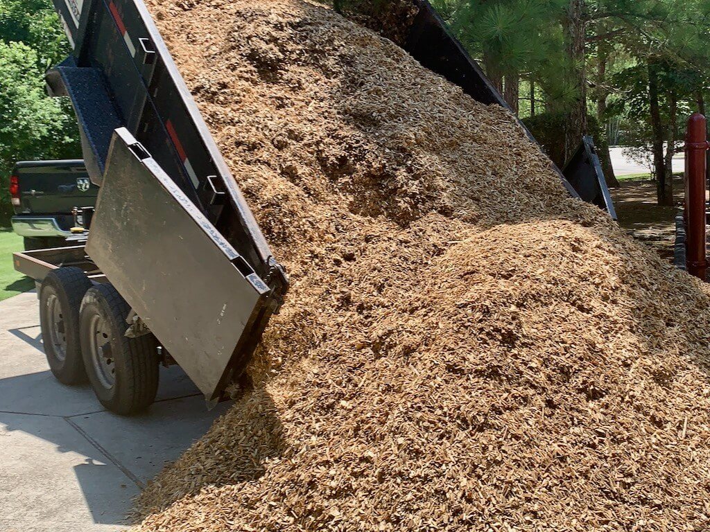 Dump trailer unloading a pile of fresh landscape mulch on a driveway